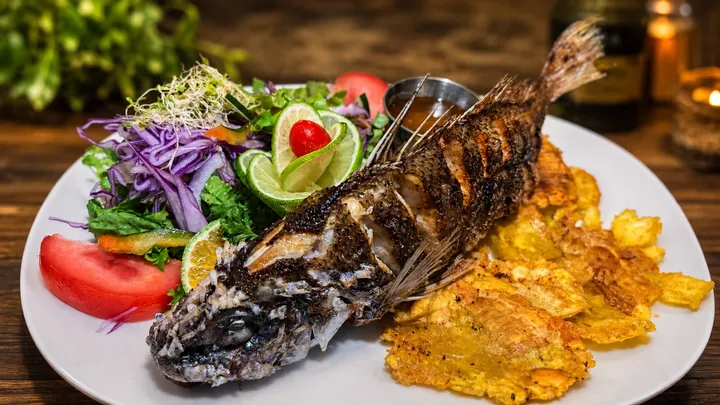 Pescado entero dorado con ensalada fresca, limón y patacones